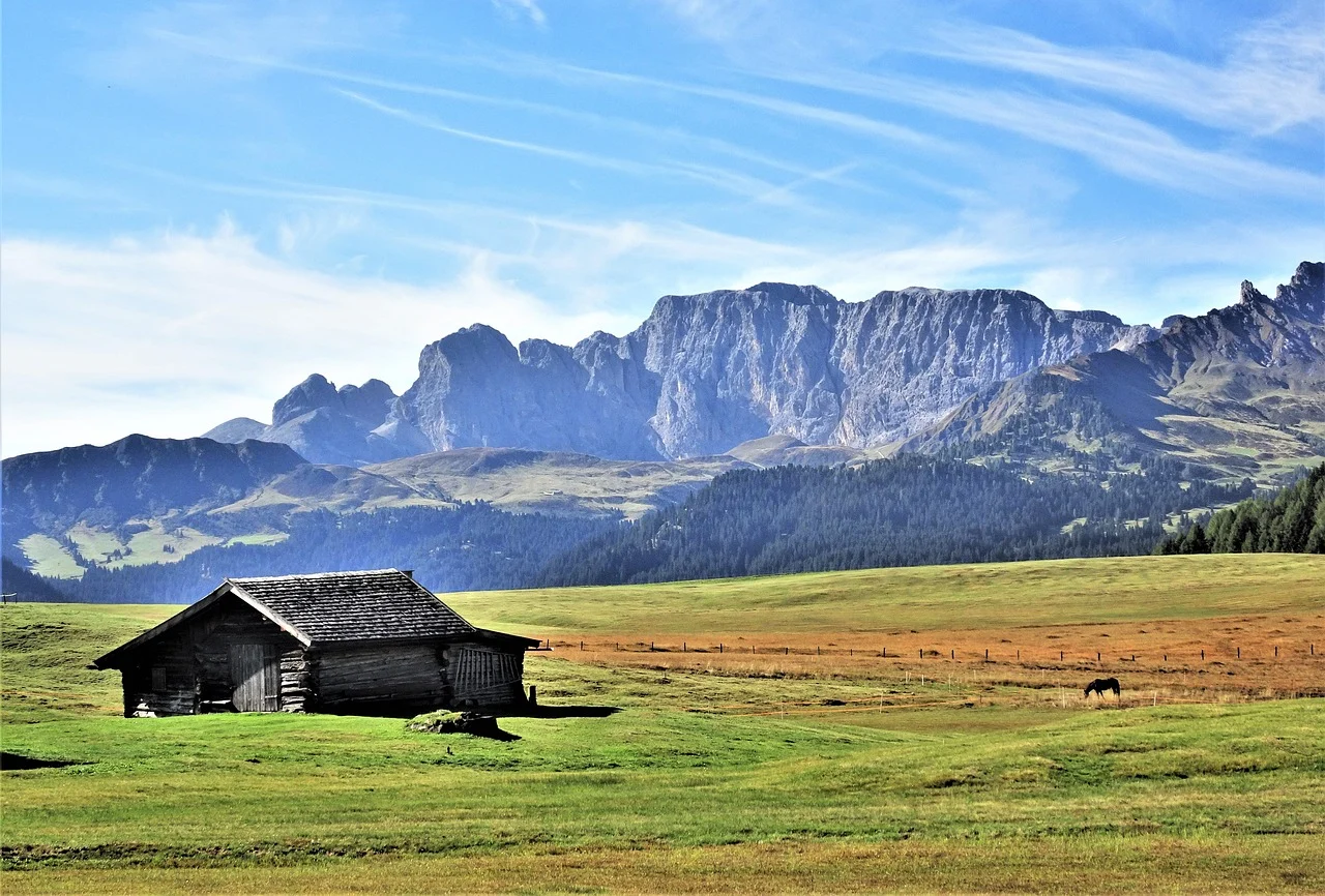Almhütte auf einer grünen Wiese vor den Felsgipfeln der Dolomiten