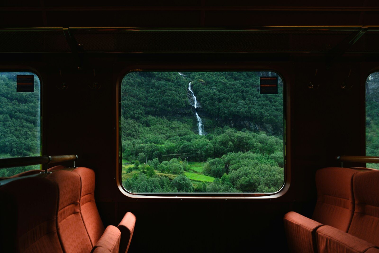 Blick aus dem Zugfenster auf eine grüne Berglandschaft mit Wasserfall