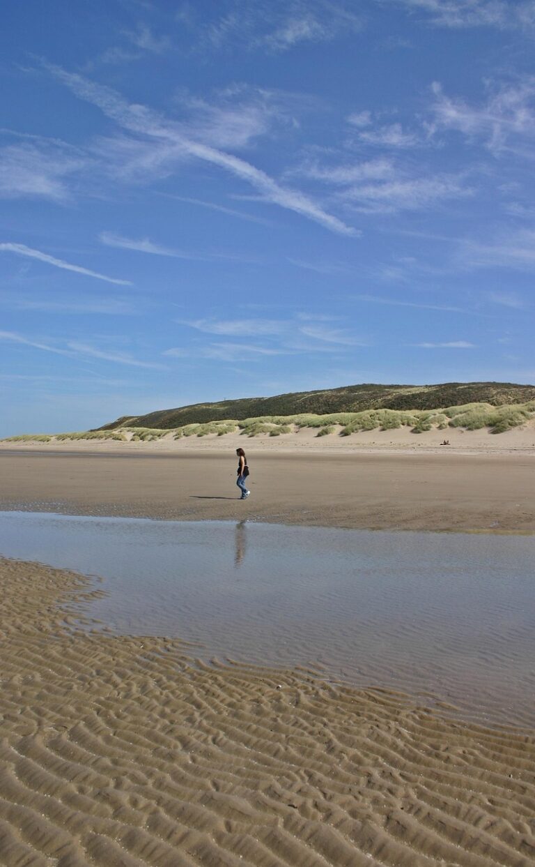 Frau geht bei Ebbe über einen breiten Sandstrand mit Dünen in Zeeland, Landschaftsfoto der Gegend, nicht die Unterkunft